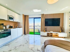 Ein modernes Hotelzimmer mit einer Küche, einem großen Fernseher und einem Balkon mit Blick.