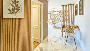 A hotel room with a wooden panel wall, a bed with a white bedspread, a dining area with a table and chairs, and a wall with tropical wallpaper. - Luxury studio, sea view in Tenerife (Playa Paraiso)