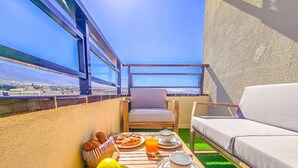 A balcony with a table set for breakfast, a sofa, and a view of the city. - Luxury studio, sea view in Tenerife (Playa Paraiso)