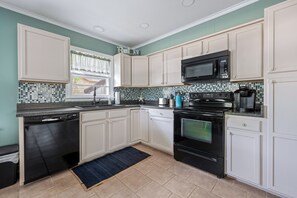 A kitchen with white cabinets, a black dishwasher, a black stove, a microwave, and a coffee maker.