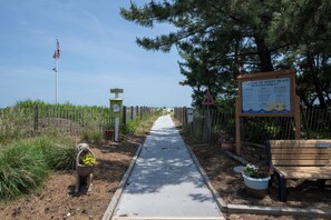A pathway leading to a beach area with a wooden bench and a signboard.