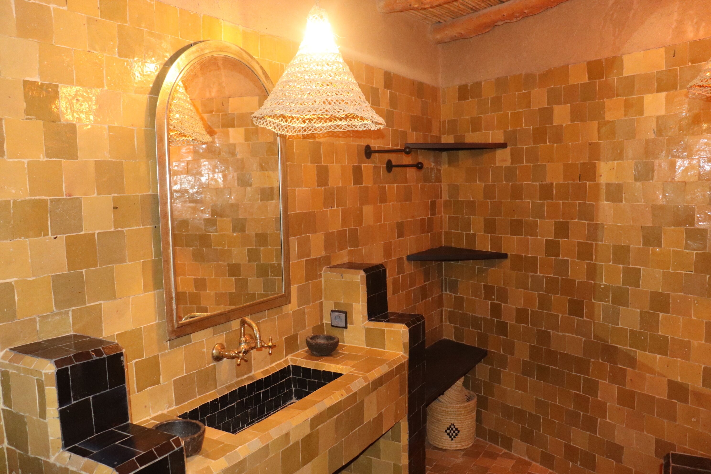 Un baño con pared de azulejos, un lavamanos, un espejo y una lámpara colgante.
