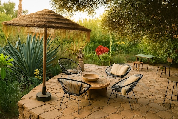An outdoor patio with stone flooring, a thatched umbrella, and modern wicker chairs.