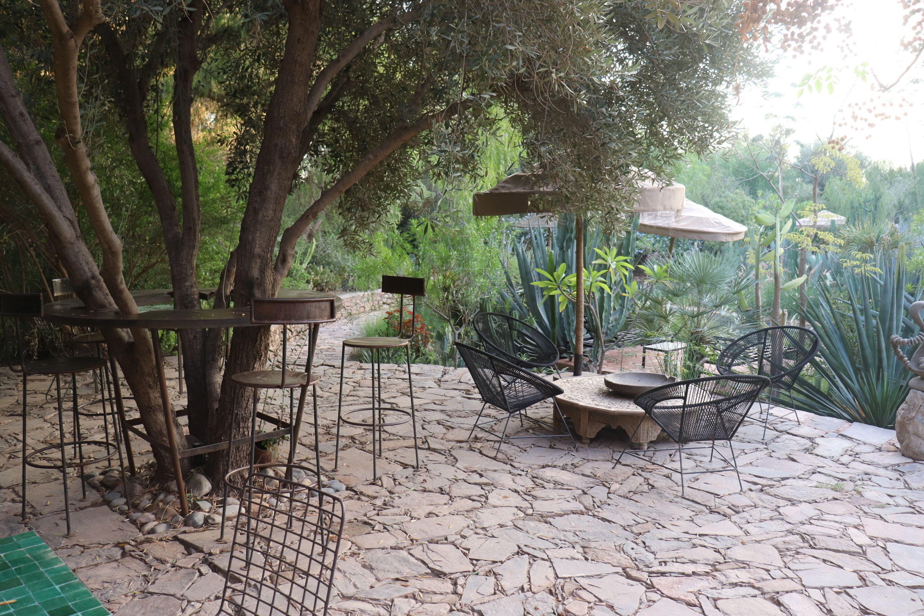 Un patio al aire libre con piso de piedra, sillas de metal, una mesa y un árbol.
