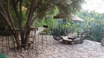Un patio al aire libre con piso de piedra, sillas de metal, una mesa y un árbol.