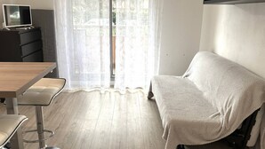 Et værelse med sofa, bord, fjernsyn på et skab og et vindue med gardiner.