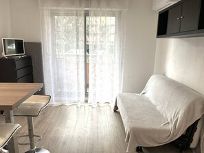 Ein Zimmer mit einer Couch, einem Tisch, einem Fernseher auf einer Kommode und einem Fenster mit Vorhängen.