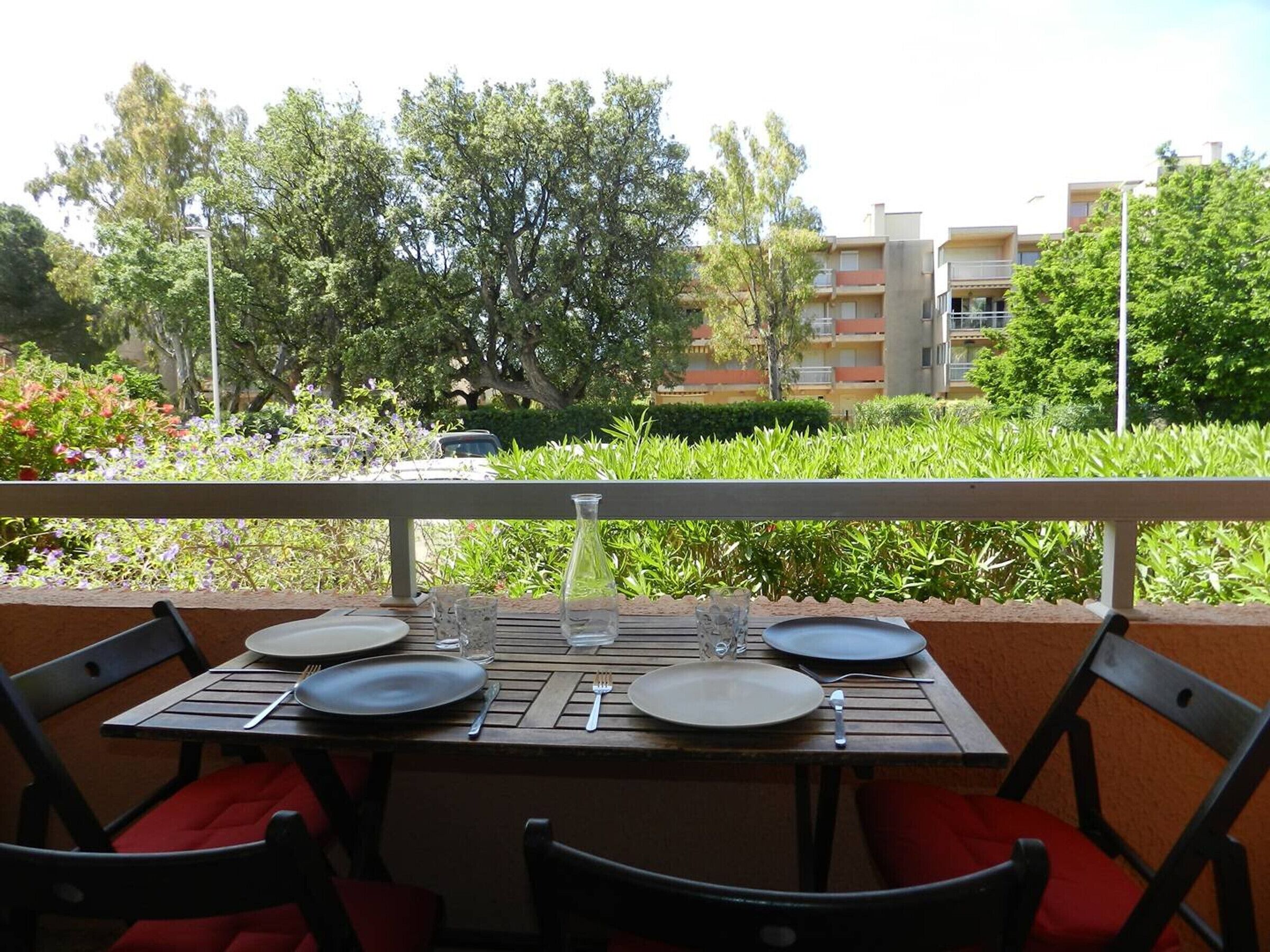 Un área de comedor al aire libre con una mesa dispuesta para cuatro personas, rodeada de vegetación y vistas a edificios.