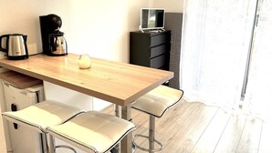 Et lille tekøkken med kaffemaskine, elkedel og et fjernsyn på et skab. To barstole og et træbord.
