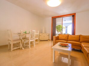 A living room with a dining table, two chairs, a sofa, a coffee table, and a window with curtains.