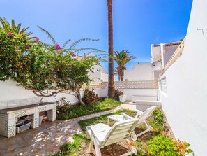Un patio con una parrilla, mobiliario exterior y una pared blanca.