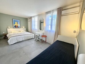 Ein Schlafzimmer mit Bett, Schreibtisch, Stuhl, Spiegel und einem Fenster mit Vorhängen.