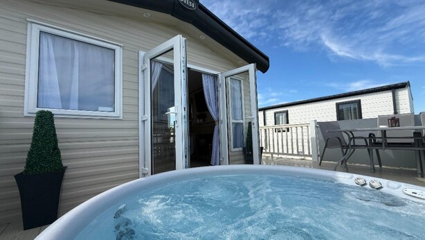 A hot tub in front of a mobile home with a patio area and a small table. - Fantasy Island H12 Caravan With Hot Tub (Skegness)