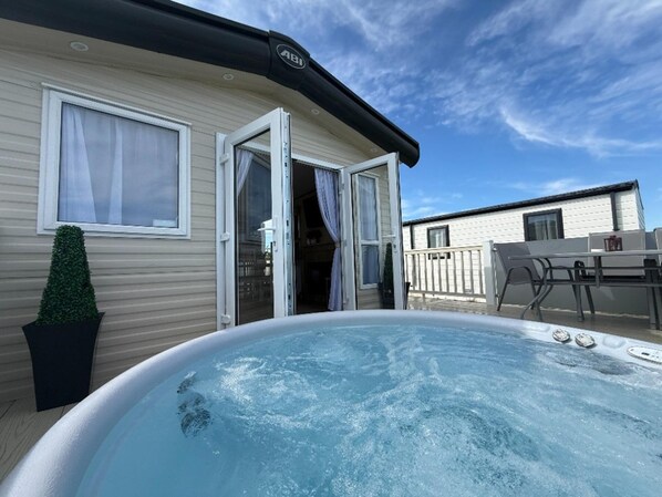 A hot tub in front of a mobile home with a patio area and a small table. - Fantasy Island H12 Caravan With Hot Tub (Skegness)