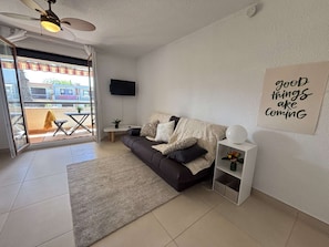 Ein modernes Wohnzimmer mit Sofa, Flachbildfernseher, Deckenventilator, einer Schiebetür zum Außenbereich und einem motivierenden Wandbild.