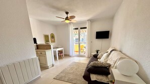 A modern living room with a sofa, a dining area with a table and chairs, a kitchen area with a counter, and a ceiling fan. - Renovated studio, terrace - 2 guests (Argelès-sur-Mer)