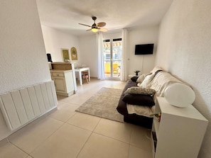 Ein modernes Wohnzimmer mit einer Couch, einem Essbereich mit Tisch und Stühlen, einer Küchenzeile mit Arbeitsplatte und einem Deckenventilator.