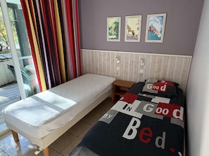 A bedroom with a single bed, a small table, a window with curtains, and three framed pictures on the wall. - Charming apartment with terrace - 4 guests (Moliets-et-Maa)