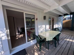 A covered patio with a table and chairs, a sliding glass door, and a wooden deck. - Charming apartment with terrace - 4 guests (Moliets-et-Maa)