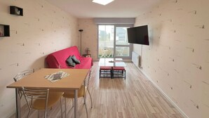 Ein kompakter Wohnraum mit Esstisch, einem roten Sofa, einem an der Wand montierten Fernseher und Blick durch ein großes Fenster.