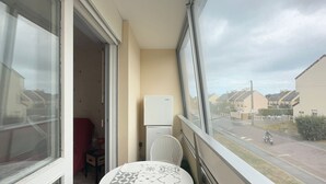 Ein Balkon mit Tisch, Stuhl, Kühlschrank und Blick auf eine Straße mit Häusern und einem Motorradfahrer.