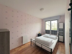 A bedroom with a bed, a radiator, a window, and a door. - Cozy apartment near the sea - 4 guests (Courseulles-sur-Mer)