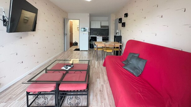 Ein modernes Wohnzimmer mit einem roten Sofa, einem Couchtisch mit Glasplatte und einem an der Wand befestigten Fernseher.