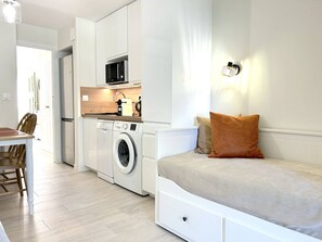 A compact kitchen with a washing machine, a microwave, and a dining area with a table and chairs.