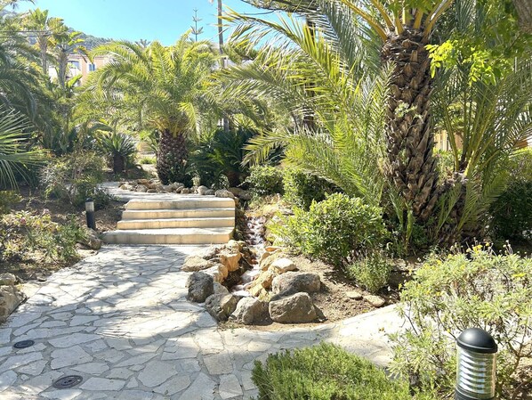 A stone pathway leading through a garden with palm trees and rocks.