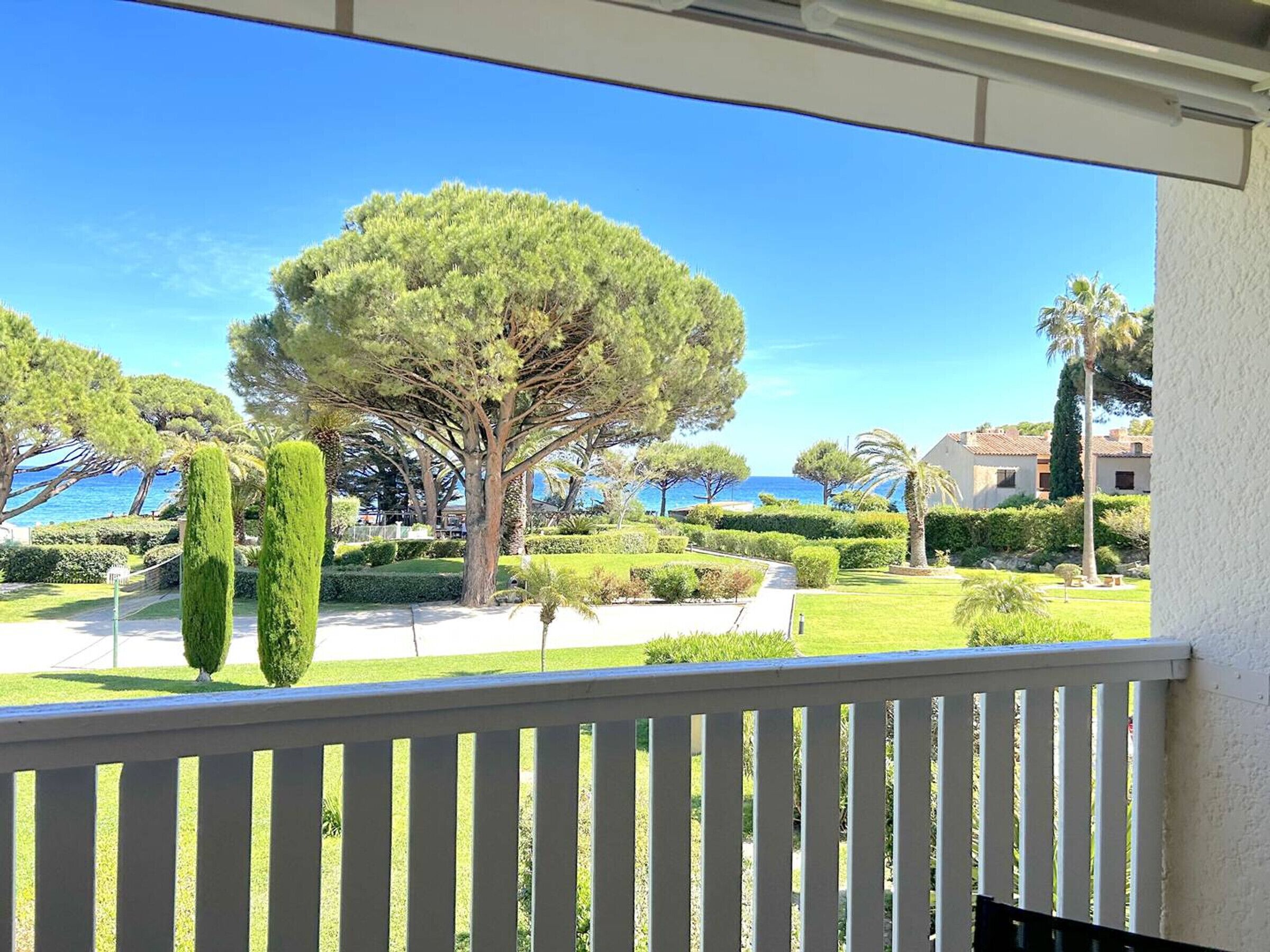 Un balcone con vista su un giardino curato, un albero grande e un edificio con tetto in tegole sullo sfondo.
