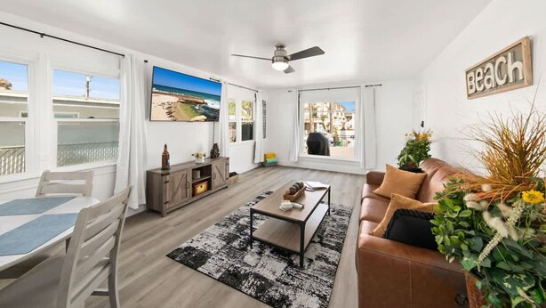 Un salon moderne avec vue sur la plage, un ventilateur de plafond et un panneau décoratif repr ésentant une plage accroché au mur.