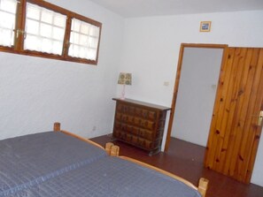 Ein Schlafzimmer mit Bett, Kommode, Fenster und Tür.
