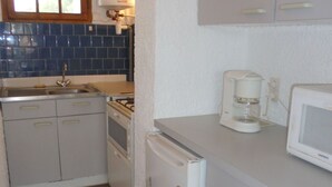 Kompakti keittiö, jossa on jääkaappi, mikroaaltouuni, kahvinkeitin ja liesi.