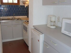 A compact kitchen with a refrigerator, microwave, coffee maker, and a stove. - Garden-side apartment - 4 guests (Argelès-sur-Mer)