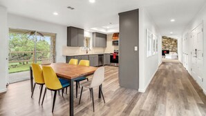 Una cocina moderna con comedor, ventanas amplias y una pared de piedra al fondo.