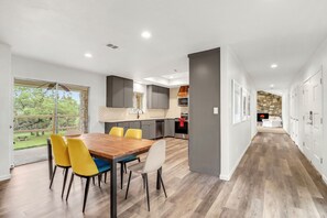 A modern kitchen with a dining area, large windows, and a stone wall in the background. - 16 Private Acres Near Wimberley Square | Hot Tub & Room for Groups (Wimberley)