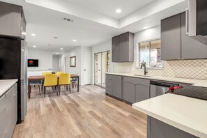 A modern kitchen with grey cabinets, a dishwasher, and a dining area with yellow chairs. - 16 Private Acres Near Wimberley Square | Hot Tub & Room for Groups (Wimberley)