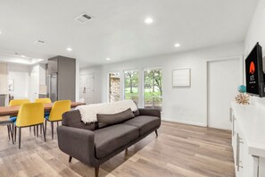 A modern living room with a gray sofa, yellow chairs, a wooden dining table, and a kitchen area in the background. - 16 Private Acres Near Wimberley Square | Hot Tub & Room for Groups (Wimberley)