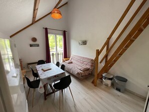Ein Zimmer mit Esstisch, Stühlen, einer Couch, einem Fenster mit Vorhängen, einer Treppe und einem Mülleimer.