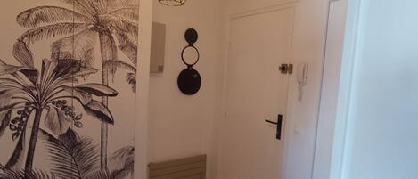 Um corredor com uma porta, um luminário fixado na parede e uma arte na parede com palmeiras.