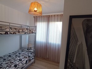 A bunk bed room with a hanging light fixture, a window with curtains, and a framed picture on the wall. - Ground floor apartment - 4 guests (Courseulles-sur-Mer)