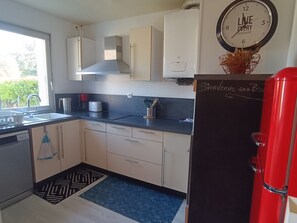 A kitchen with a blackboard, a red refrigerator, and a clock on the wall. - Ground floor apartment - 4 guests (Courseulles-sur-Mer)