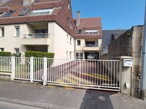 A multi-story residential building with balconies, a gated entrance, and a parking area. - Ground floor apartment - 4 guests (Courseulles-sur-Mer)