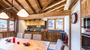 Un interior de fusta amb taula de dinar, cadires, zona de cuina i televisió.
