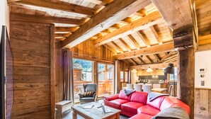 Un interior de fusta acollidor amb un sofà de pell vermella, una taula de dinar de fusta i una zona de cuina visible a través d'una porta oberta.