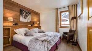 Ein gemütliches Schlafzimmer mit einem hölzernen Kopfteil, einem großen Bett mit weißer und brauner Decke, einem kleinen Schreibtisch und einem Stuhl.