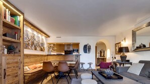 Ein modernes Wohnzimmer mit einer Wand in Holzoptik, einem Essbereich mit Hockern und einer Küche im Hintergrund.