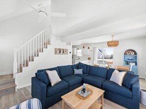 Uma sala de estar moderna com um sofá seccional, uma mesa de centro de madeira e uma escada.