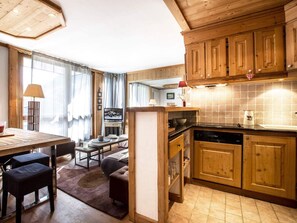 Une cuisine chaleureuse avec des meubles en bois, un coin repas avec une table et des chaises, et un espace de vie avec un canapé et un téléviseur.