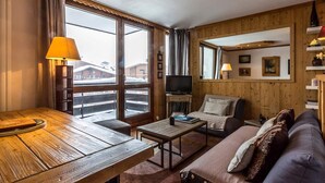 Tunnelmallinen huone, jossa on puinen pöytä, sohva, televisio ja suuret ikkunat.